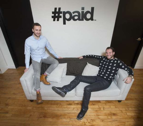 Two men on a couch and behind them the paid logo